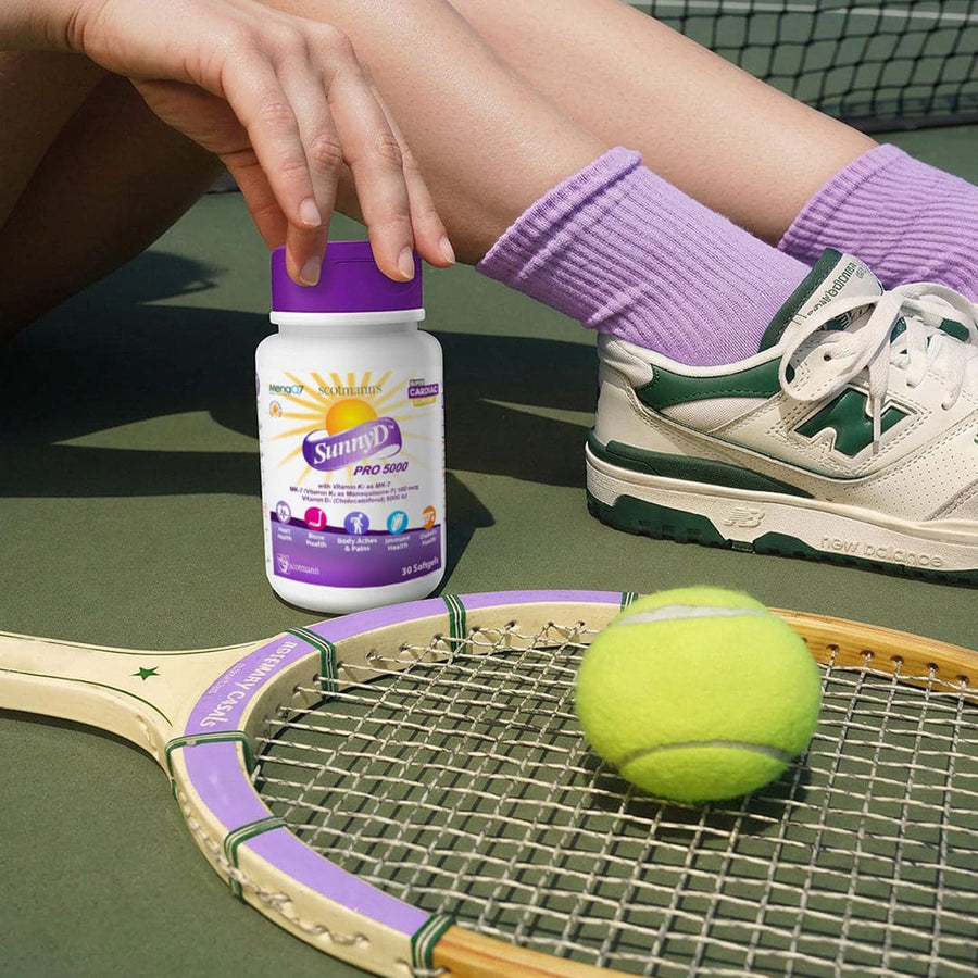 Person sitting on a tennis court with a bottle of SunnyD Pro 500, a tennis racket, and a tennis ball.