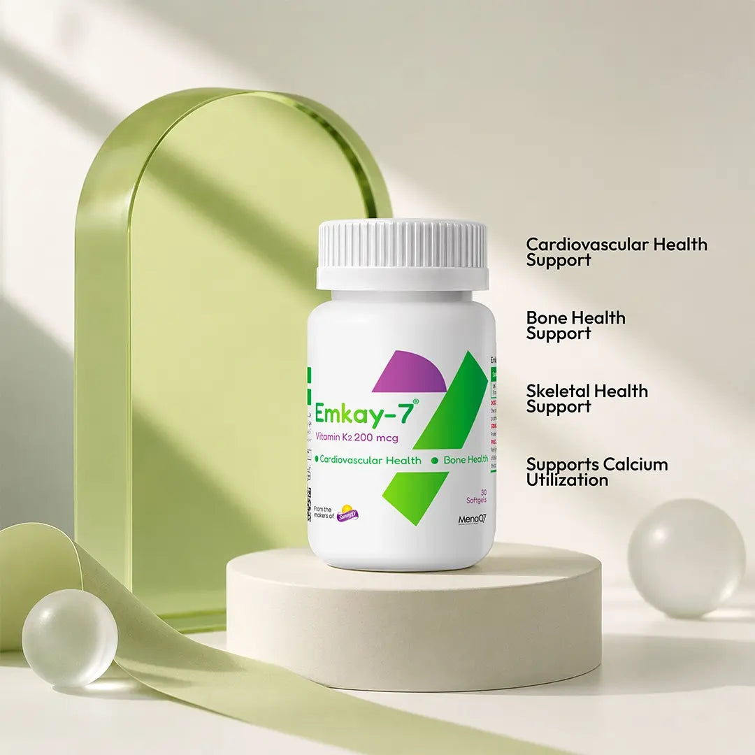 A white bottle of Emkay-7 dietary supplement with a ribbed white cap, displayed on a round pedestal. The background features a light green arch, decorative ribbons, and clear spheres, with text on the right detailing the product's health benefits: Cardiovascular Health Support, Bone Health Support, Skeletal Health Support, and Supports Calcium Utilization.