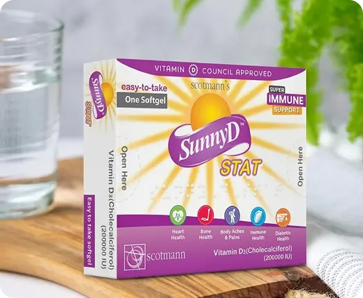 A box of Scottmann's SunnyD STAT Vitamin D3 softgel capsules, displayed on a wooden surface with a glass of water and green leaves in the background.