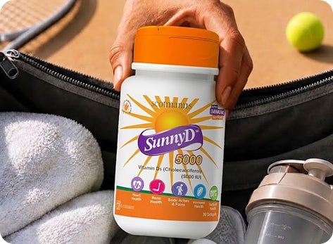 A hand holding a bottle of Commanzy SunnyD 5000 Vitamin D3 supplement, positioned over an open black bag with a towel and a shaker bottle nearby.